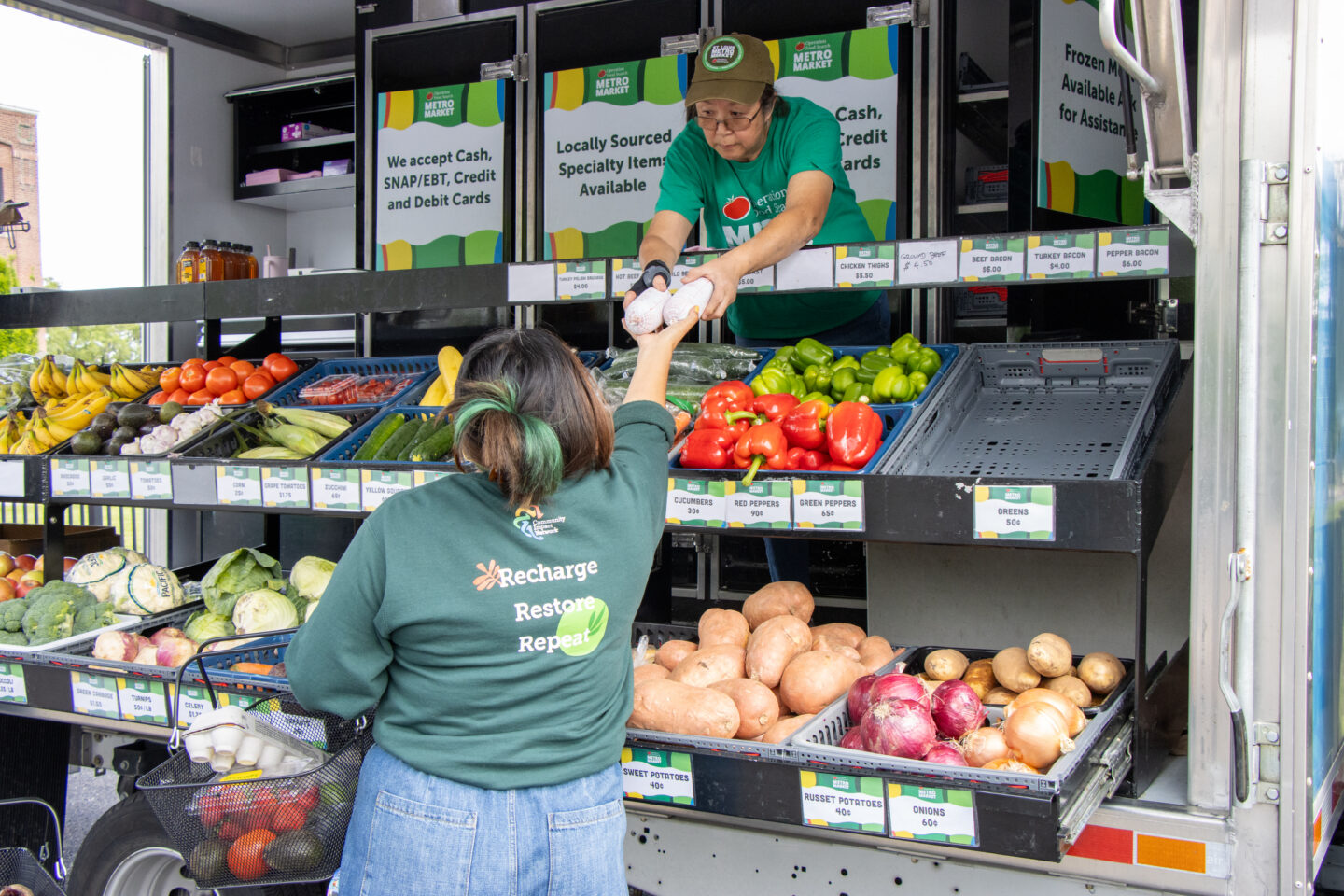 Vendor in a green shirt hands eggs to a customer at a mobile produce stand with fresh vegetables nearby.