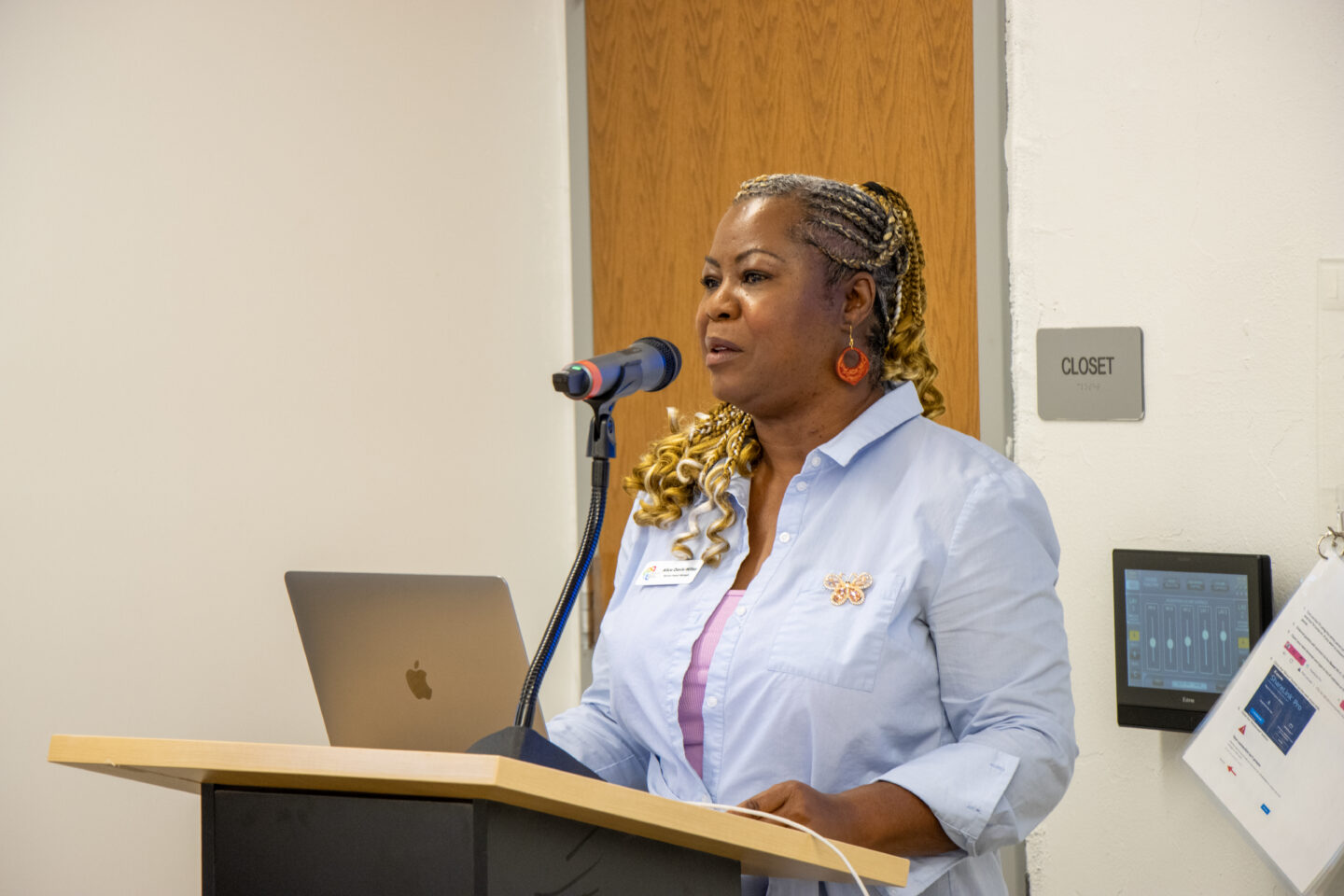 Woman speaking at a podium with a microphone and laptop in front of her, delivering a talk.