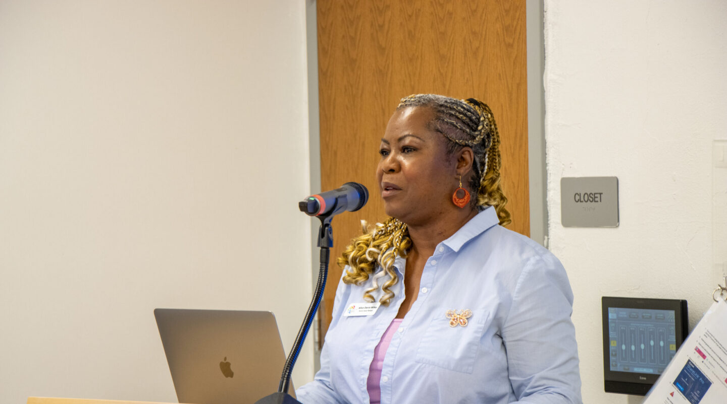 Woman speaking at a podium with a microphone and laptop in front of her, delivering a talk.